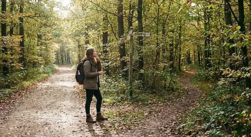 Kobieta stojąca na rozdrożu leśnej ścieżki, symbolizująca moment podejmowania ważnych życiowych decyzji.