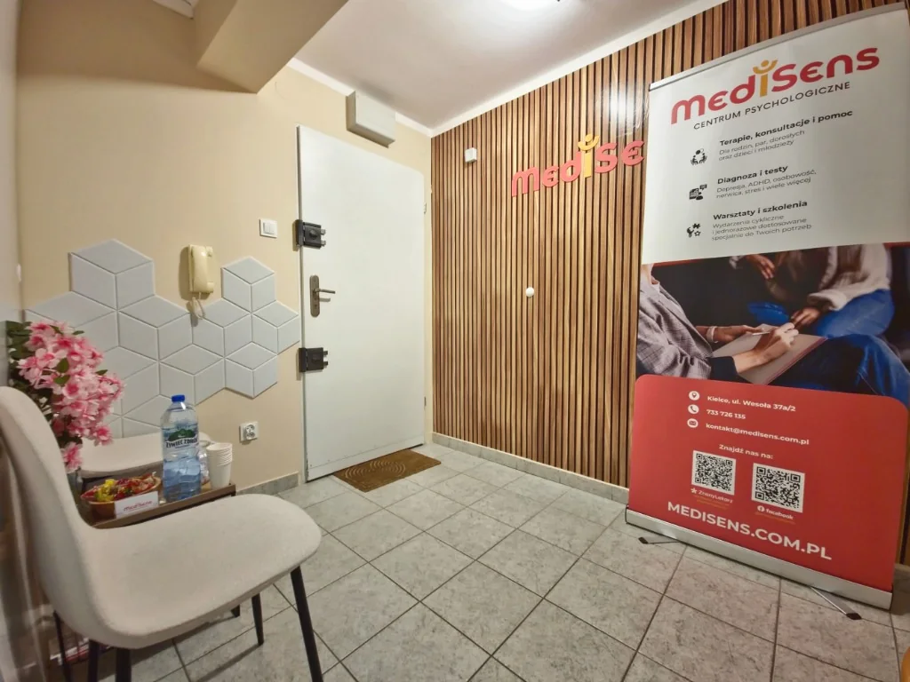 Strefa recepcji i poczekalnia - Centrum MediSens Kielce Strefa wejściowa i recepcja Centrum Psychologicznego MediSens w Kielcach ze ścianą z logo i materiałami informacyjnymi